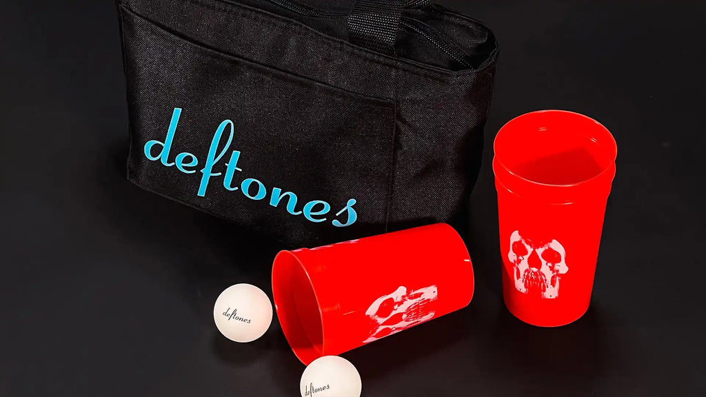Black bag with blue ’deftones’ lettering, accompanied by red cups and white ping-pong balls.